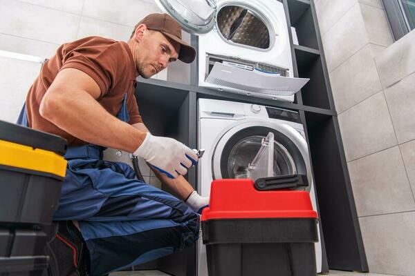 a man from laundry rescue in a brown shirt and blue pants working on a washing machine